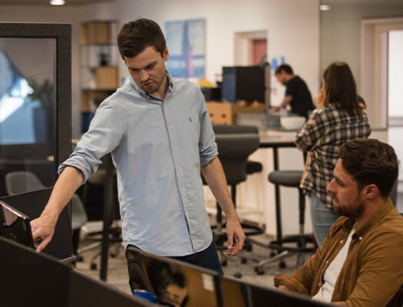 Man standing showing another man something on computer