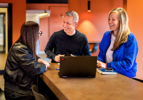 Team members collaborating around a laptop in a modern workspace.